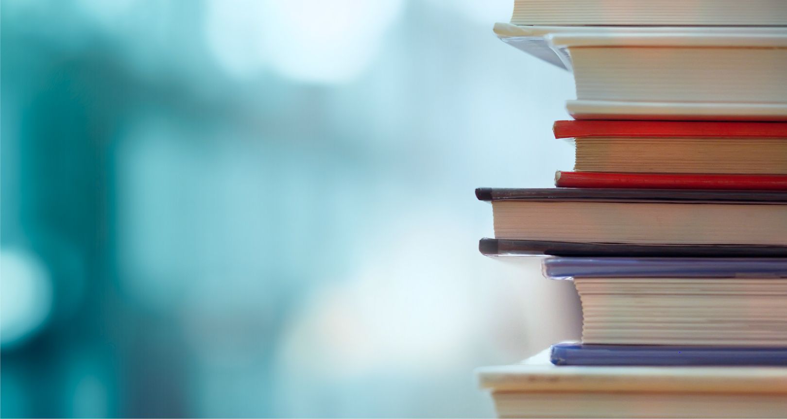 Eine Nahaufnahme eines ordentlich gestapelten Stapels bunter Bücher mit unscharfem, weichgezeichnetem Hintergrund.